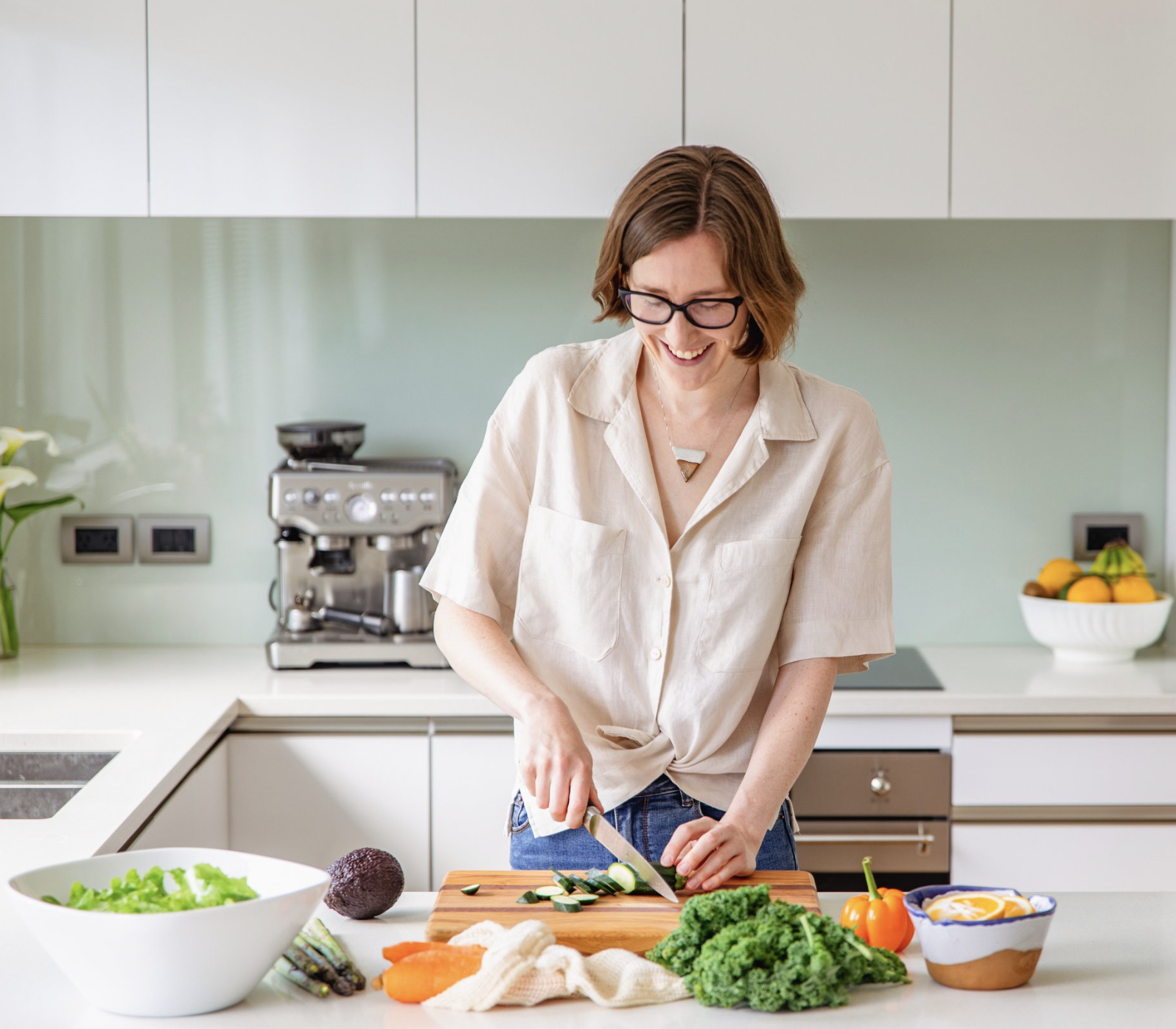 Image of Lana, a Naturopath chopping vegetables in a brightly lit kitchen counter with a smile on her face.